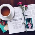 opened book with pink flower on top near filled ceramic mug