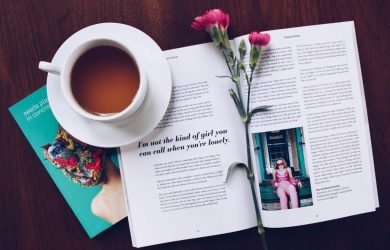 opened book with pink flower on top near filled ceramic mug