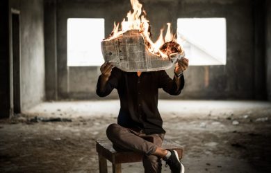 man sitting on chair holding newspaper on fire