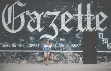 woman standing and leaning on Gazette painted wall during daytime