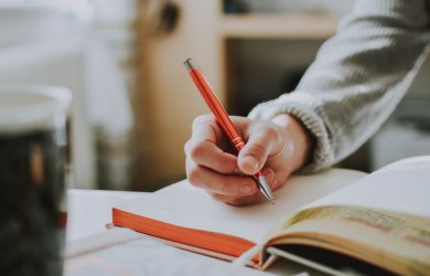 person holding on red pen while writing on book