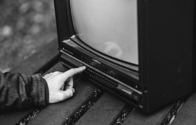 Black and white of unrecognizable male pressing buttons on old fashioned television placed on wooden table in nature on blurred background