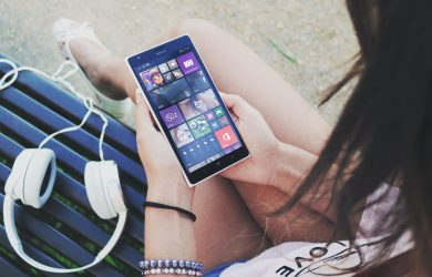Woman Holding Turned Smartphone While Sitting on Bench Close-up Photography