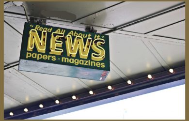 From below of illuminated signboard with news papers magazines inscriptions hanging on metal ceiling on street