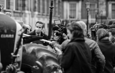 grayscale photo of man in black coat holding camera